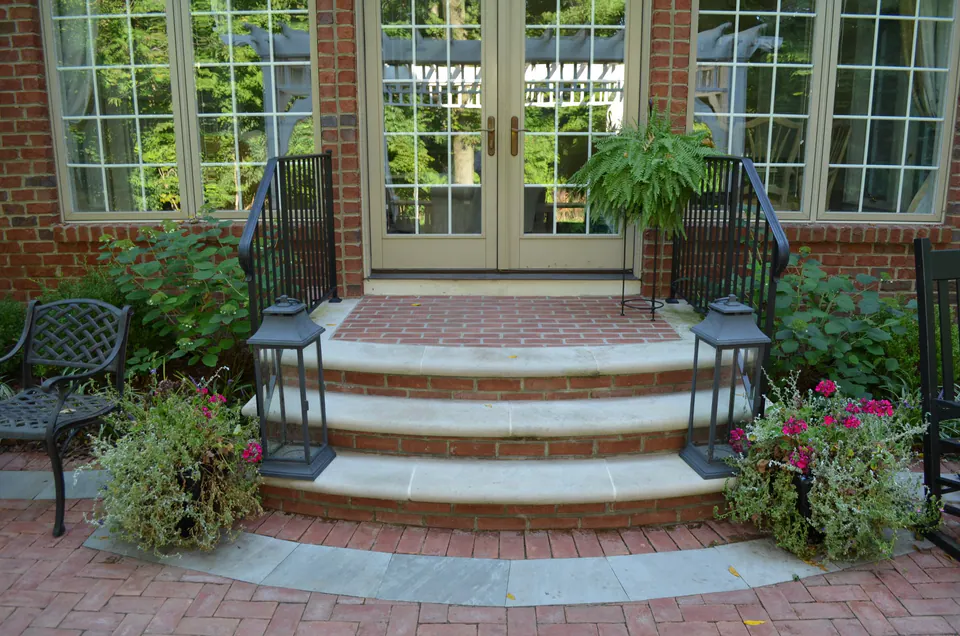 Curved stone steps with brick risers leading to French doors, with lanterns and planted pots